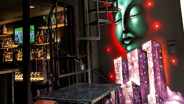 A bar area with a spiral staircase, bar stools, and a mural of a Buddha's face.