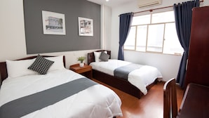 A hotel room with two beds, a small bedside table with a plant, and a window with curtains.