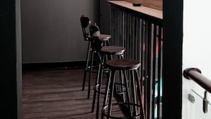 A narrow corridor with wooden flooring, a bar area with stools, and ceiling lights.