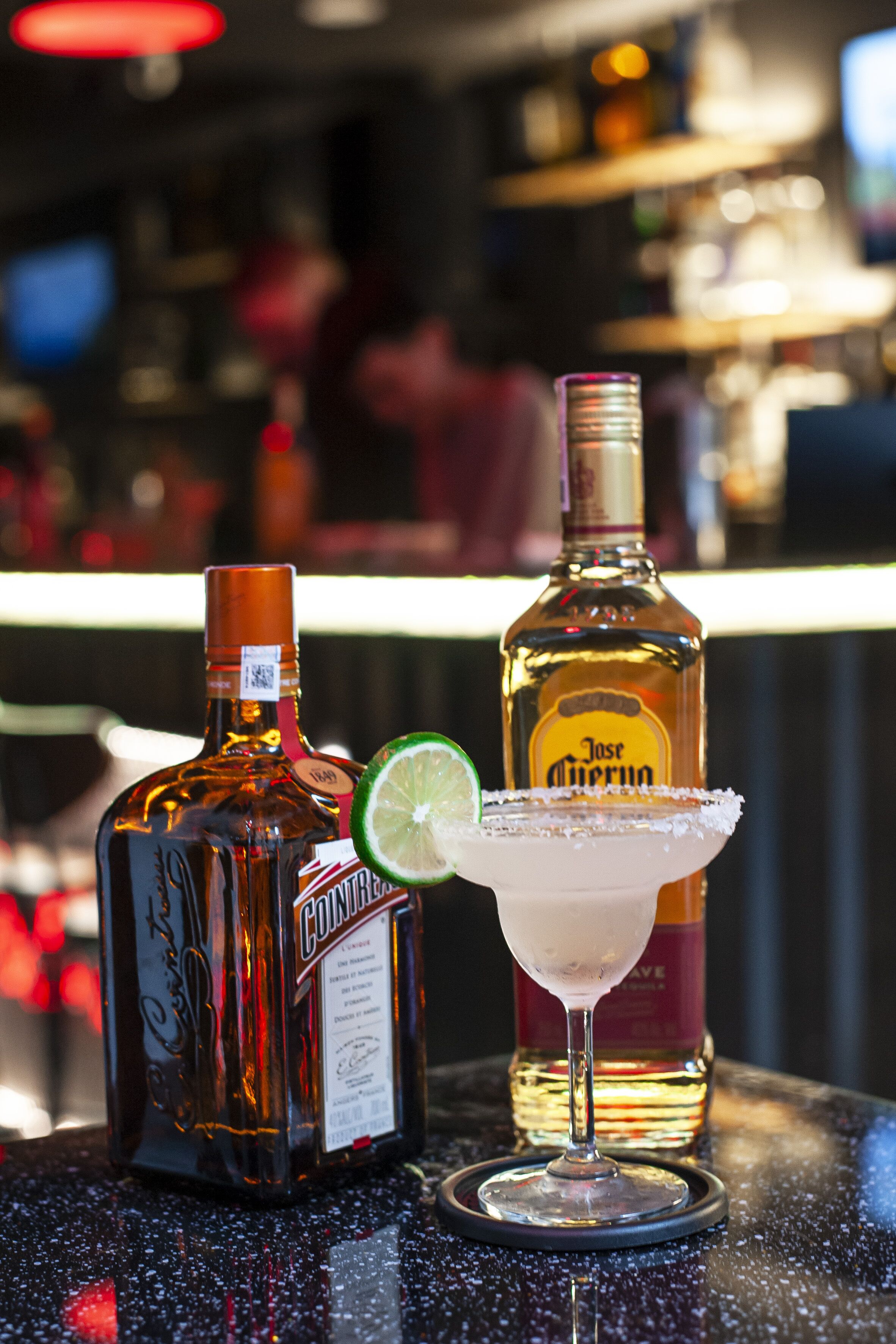 Dos botellas de licor y una copa de margarita sobre una barra.