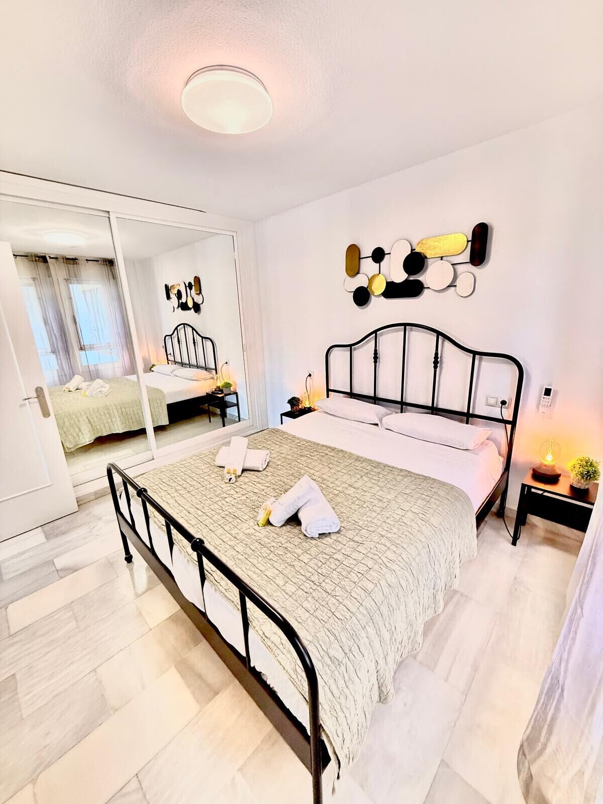 Un dormitorio con cama, mesita de noche, espejo y un adorno en la pared.