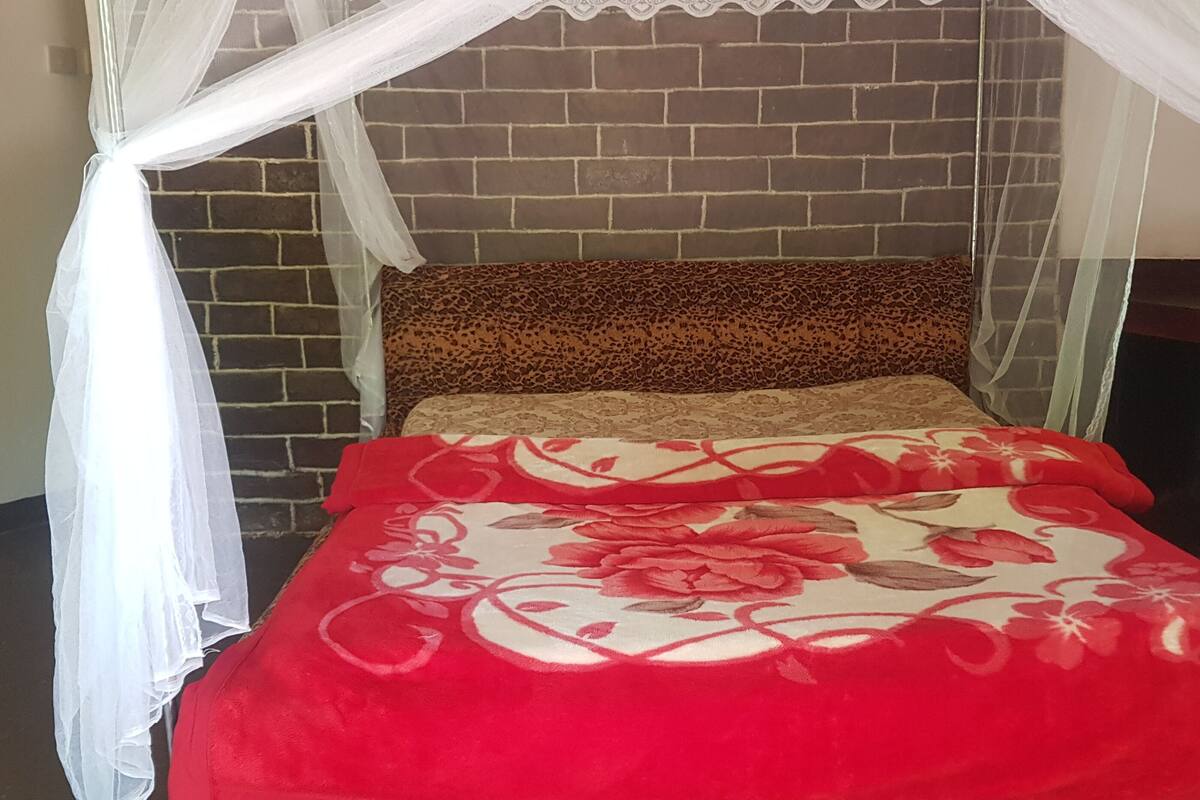 A bed with a red floral bedspread, a leopard print pillow, and white curtains.