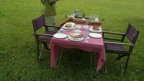 A table set outdoors with a pink tablecloth, surrounded by chairs. - Tanzanin Eco Home & Camp (Arusha)