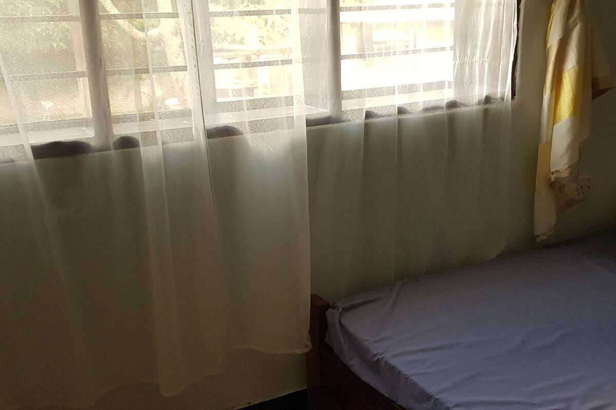 A room with a bed, a window with sheer curtains, and a radiator.