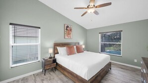 A bedroom with a bed, nightstands, a ceiling fan, and large windows.
