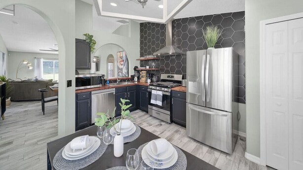 A modern kitchen with stainless steel appliances, a dining area with a table set for four, and a living room with a sofa and a TV.