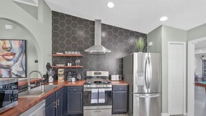 A modern kitchen with a stainless steel refrigerator, a built-in oven, and a microwave. There are wooden shelves above the stove and a sink with a faucet.