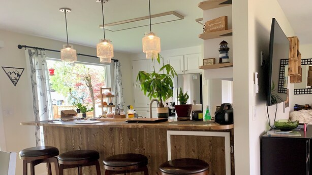 Una cocina moderna con barra, taburetes de madera, iluminación colgante y un televisor sobre un mueble bajo.