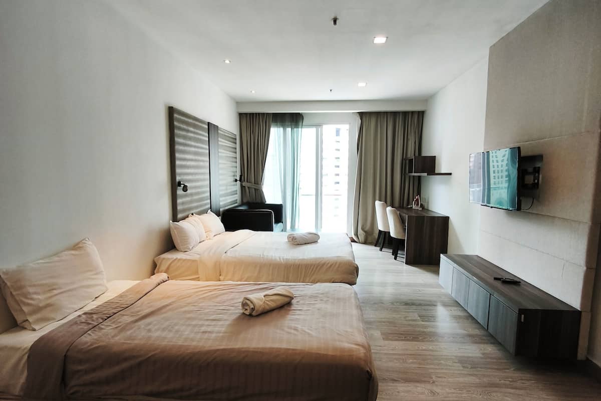 A modern hotel room with two beds, a flat-screen TV mounted on the wall, a wooden floor, and a large window with curtains.