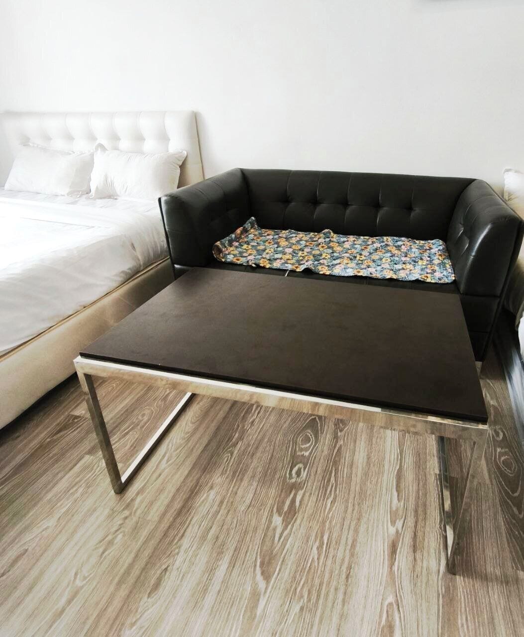 A modern room with a dark brown leather sofa, a wooden coffee table, and a white bed with a tufted headboard.