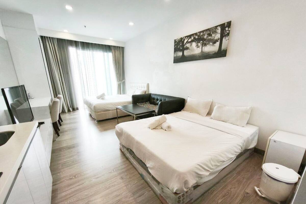 A modern hotel room with a large bed, a sofa, a desk, and a TV.