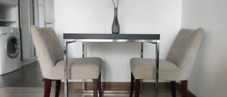 A modern dining area with a glass-top table and two upholstered chairs.