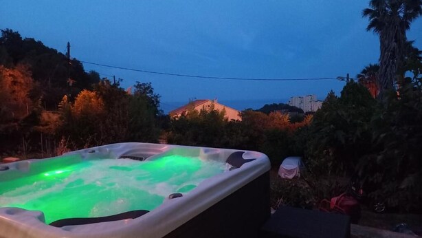 A hot tub with green lighting, surrounded by trees and a view of buildings in the background. - Location Estivale Bastia U Fiumicellu, Vue Mer. Jacuzzi, Barbecue, (Bastia)