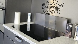 A modern kitchen with dark cabinetry, a stainless steel range hood, and a decorative wall decal that reads "Bon appétit!" - Location Estivale Bastia U Fiumicellu, Vue Mer. Jacuzzi, Barbecue, (Bastia)
