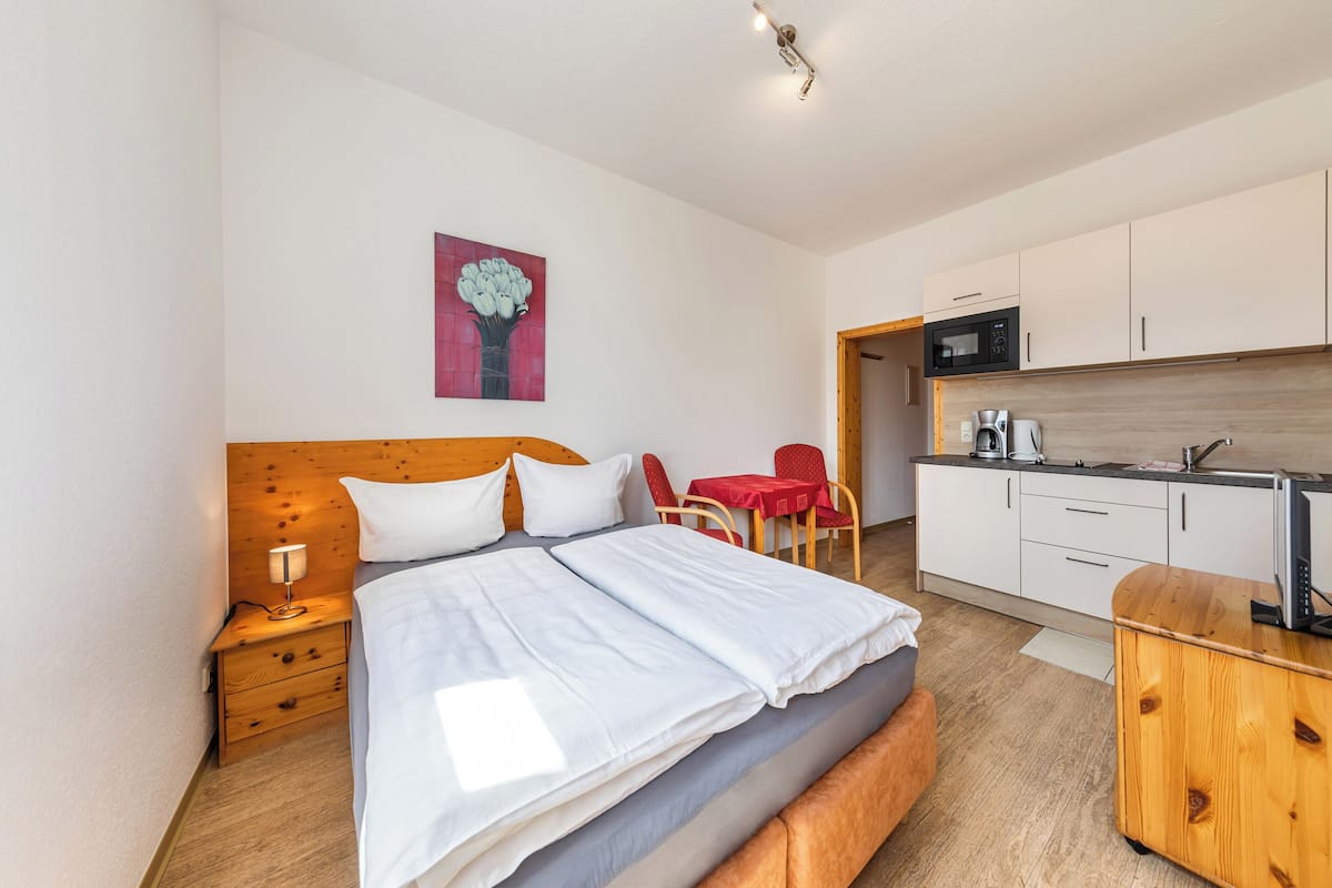 Une chambre d’hôtel avec un lit, une table de chevet, une lampe et une petite table rouge avec des chaises.