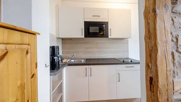 Cozinha compacta com armários brancos, micro-ondas preto e cafeteira.