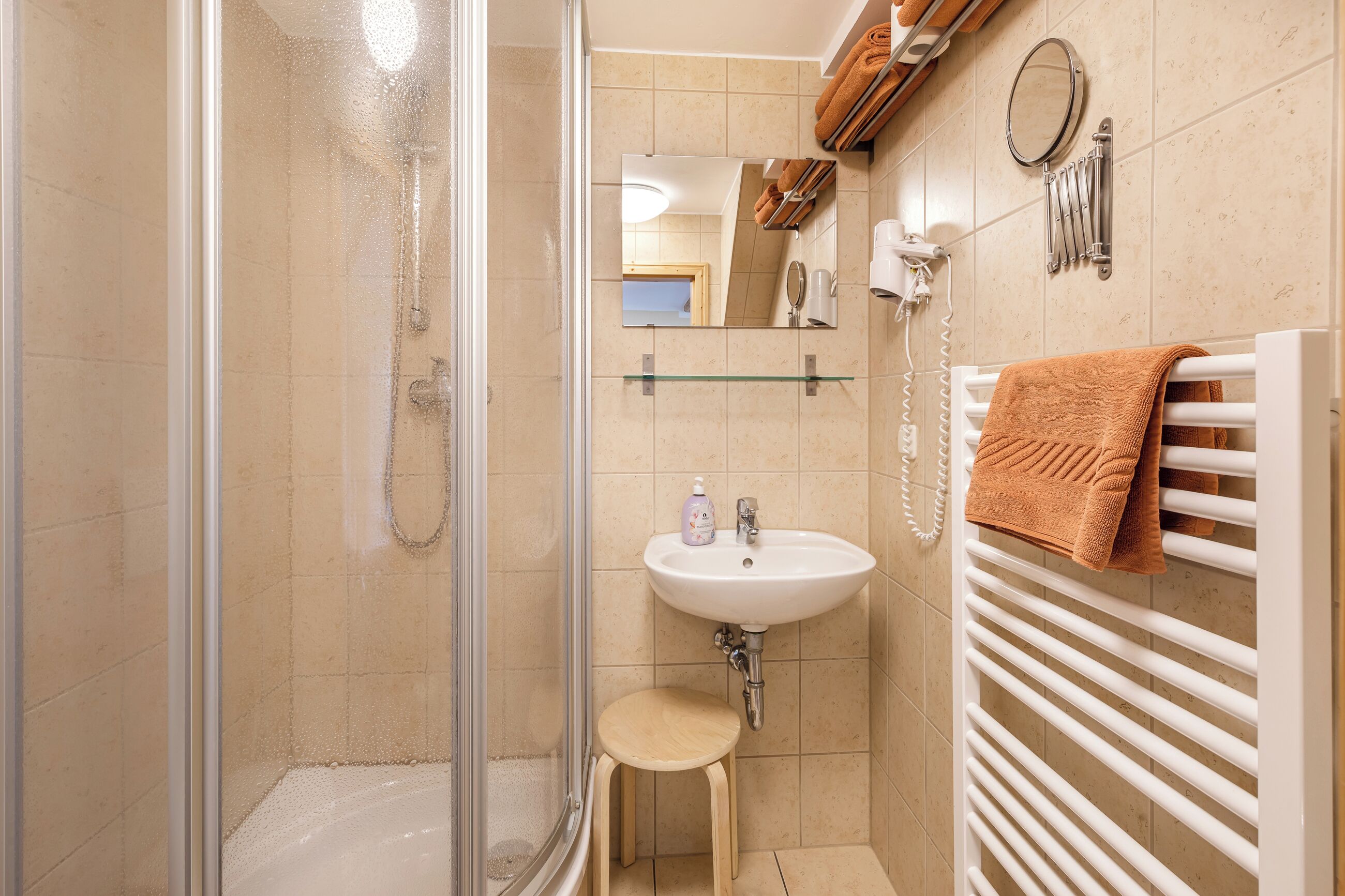 A bathroom with a glass shower enclosure, a sink with a mirror above it, and a towel rack with a towel.