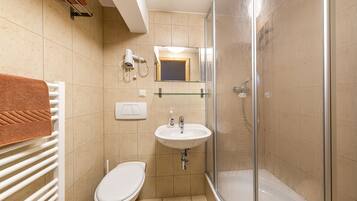 Une salle de bain avec des toilettes blanches, des carreaux beiges, une douche en verre et un lavabo blanc avec un miroir au-dessus.