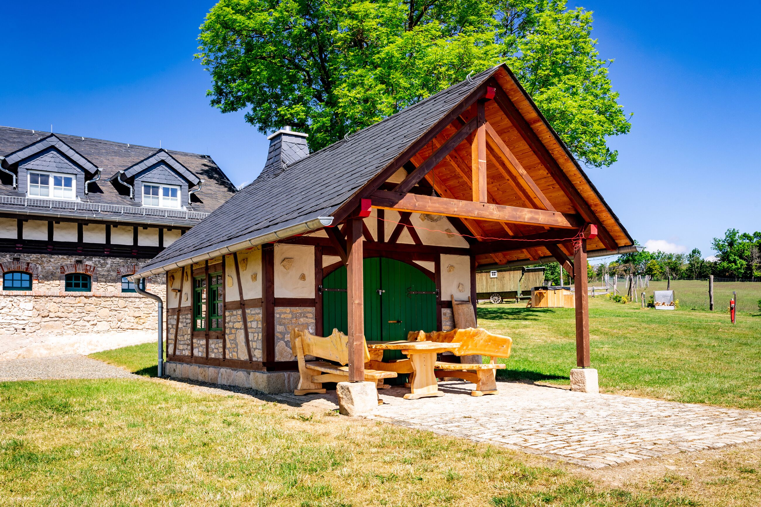 Ein rustikales Holzpavillon mit grüner Tür, Bänken und einem Picknicktisch in einer grünen Wiese.