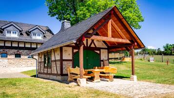 Ein rustikales Holzpavillon mit grüner Tür, Bänken und einem Picknicktisch in einer grünen Wiese.