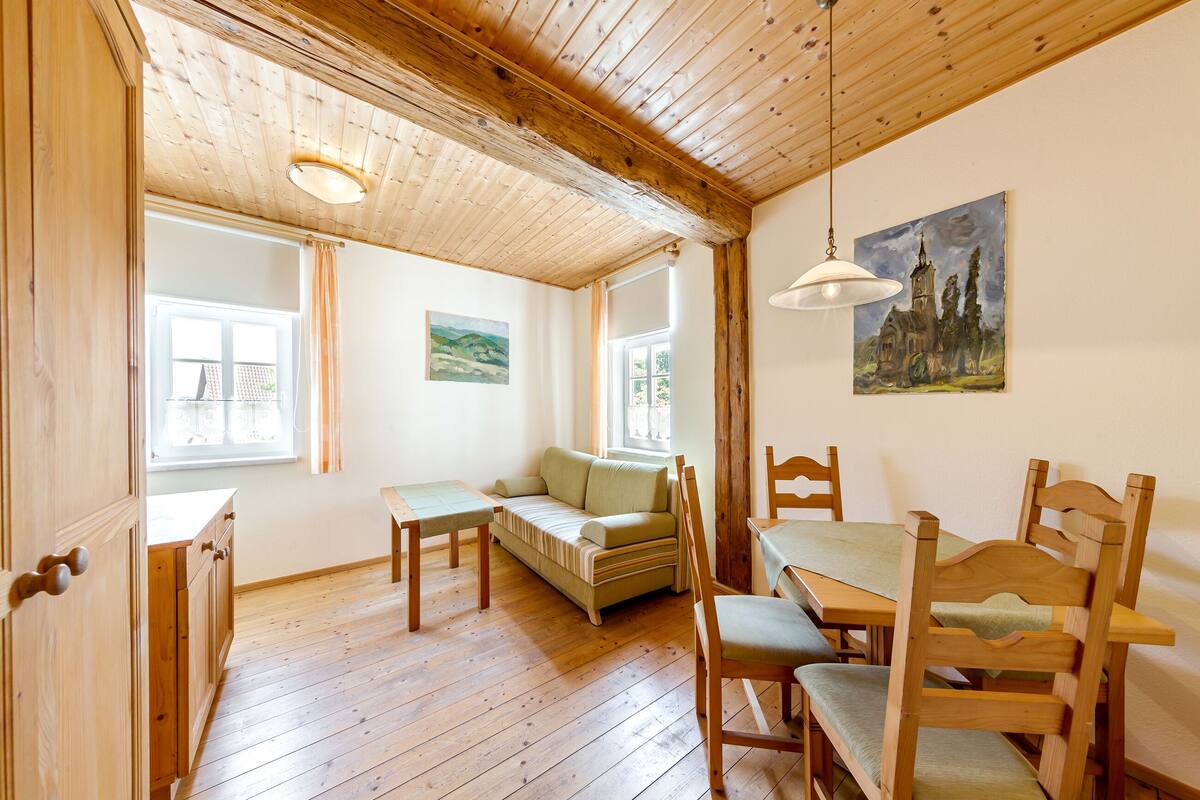 Une pièce au plancher de bois, avec un canapé, une table à manger, des chaises et un tableau accroché au mur.