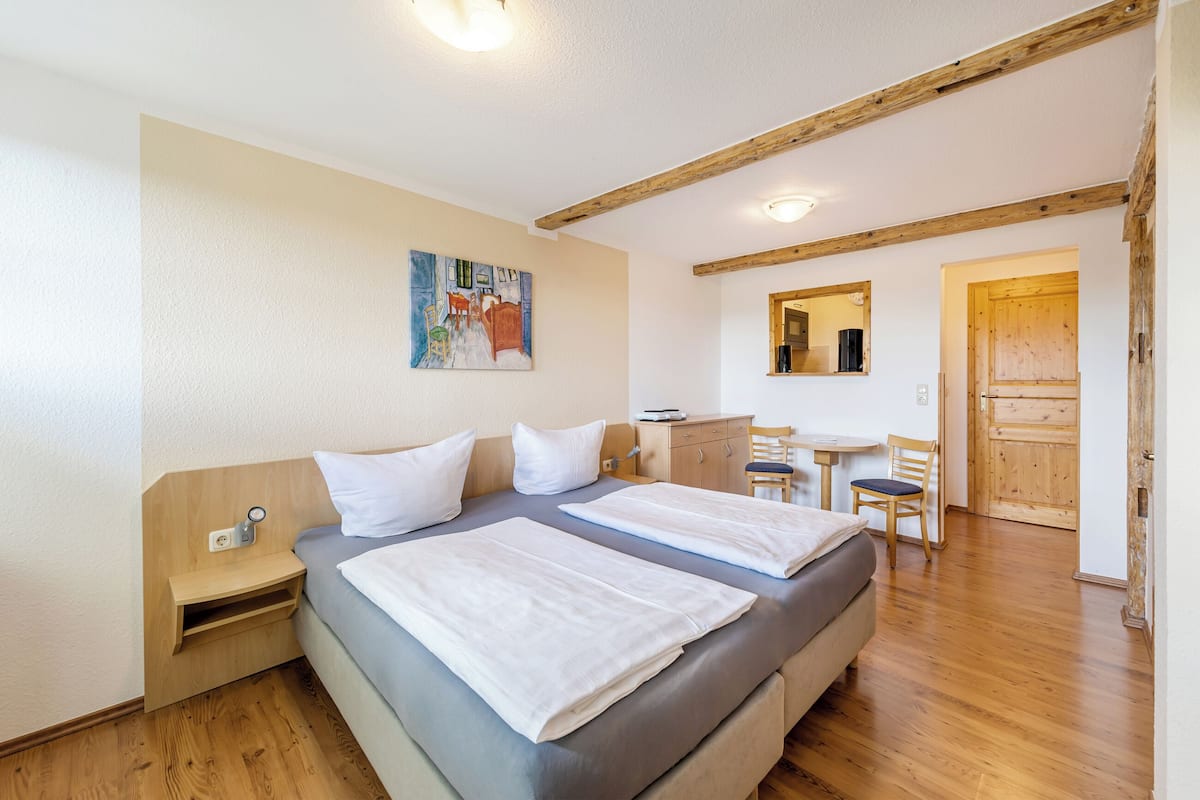 Une chambre avec deux lits, une tête de lit en bois, une table de chevet, une petite table avec des chaises et une porte en bois.