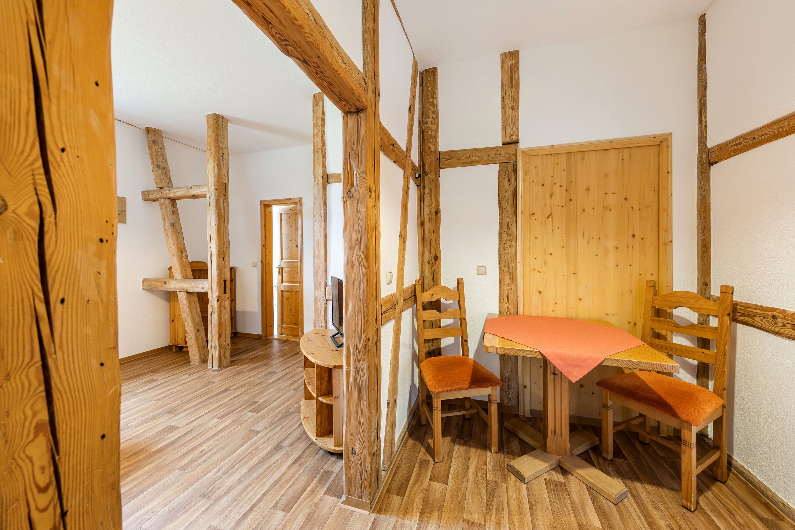 A room with exposed wooden beams, a wooden table with orange cushions, and a wooden chair.