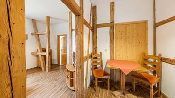 A room with exposed wooden beams, a wooden table with orange cushions, and a wooden chair.