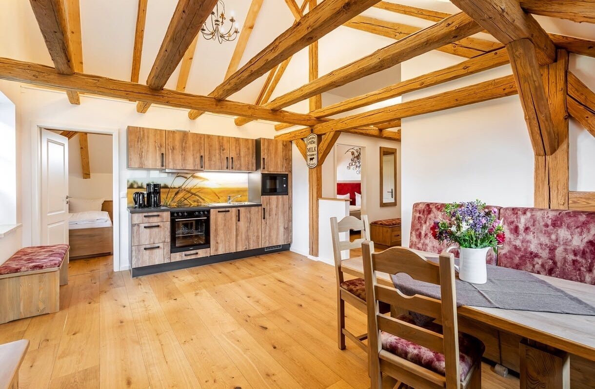 Una cucina rustica con travi in legno, un'area pranzo con una panca imbottita rossa e un piccolo angolo salotto con una panca cuscinerata.