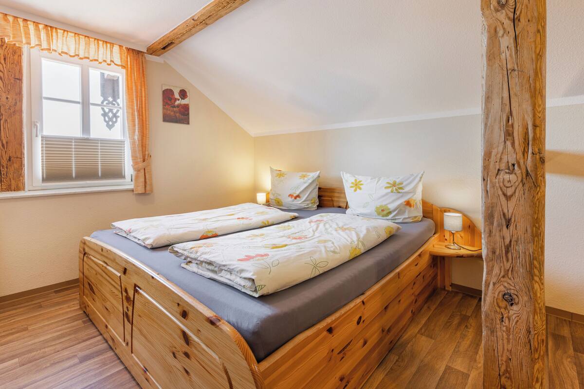 Une chambre à coucher avec un lit en bois, une fenêtre avec des rideaux, une table de chevet avec une lampe et un poteau en bois.