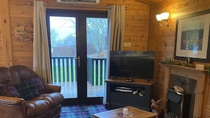 A cozy cabin interior with a plaid carpet, leather furniture, a fireplace, and a television.
