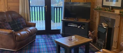 A cozy cabin interior with a plaid carpet, leather furniture, a fireplace, and a television.