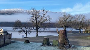 A lakeside view with a wooden deck, a rustic tree stump, and a snow-covered mountain in the background.