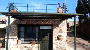 Ein Steinhaus mit einer grünen Tür und Fenstern, einer kleinen Veranda mit Blumentöpfen und einem Metallgeländer darüber.