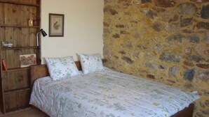 Ein Schlafzimmer mit einem hölzernen Bett, einer Steinwand und einem Holzregal mit verschiedenen Gegenständen.