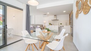 A modern kitchen with white cabinets, a stainless steel range hood, and a dining area with a glass table and white chairs. - 0069-MIMOSES Modern apartment near the beach (Empuriabrava)