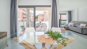 A modern living room with a glass dining table, grey curtains, a grey sofa, and a view of buildings through the glass door. - 0069-MIMOSES Modern apartment near the beach (Empuriabrava)