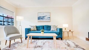 A living room with a blue sofa, a grey armchair, a wooden coffee table, a floor lamp, and a painting on the wall.