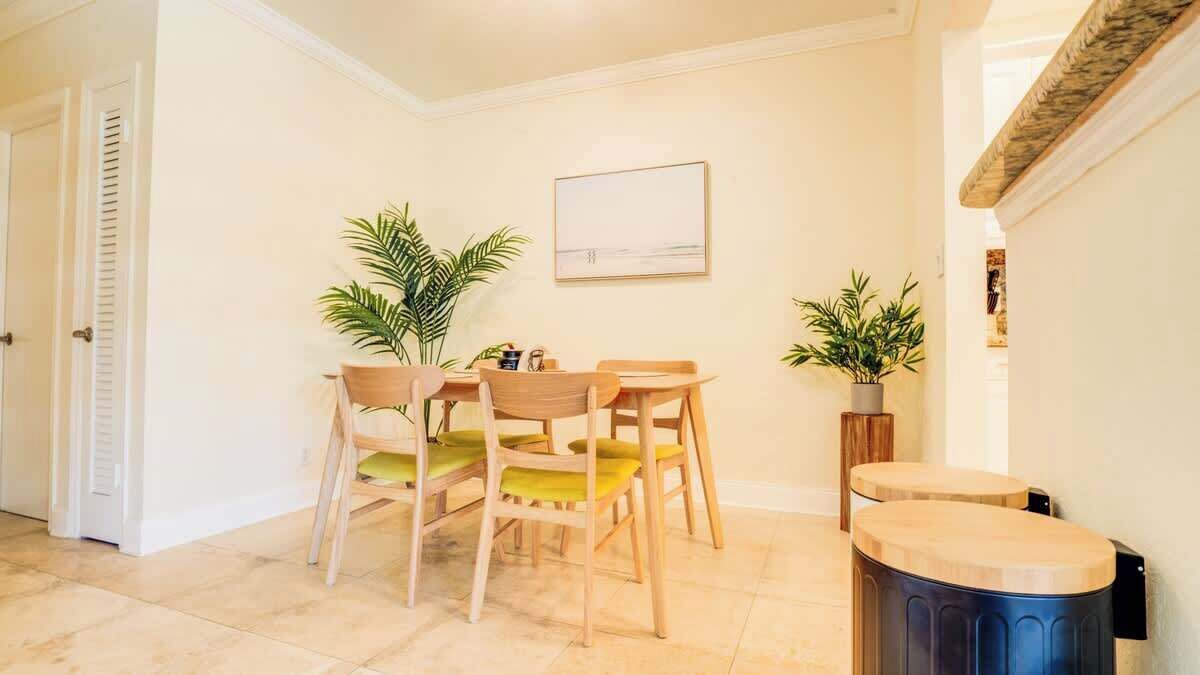 Uma área de refeições com mesa e cadeiras, uma planta em vaso e um quadro na parede.