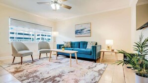 A living room with a blue sofa, two armchairs, a coffee table, a floor lamp, and a large window with blinds.