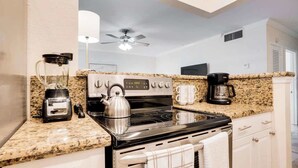 A compact kitchen with a stove, toaster, kettle, coffee maker, and a microwave.