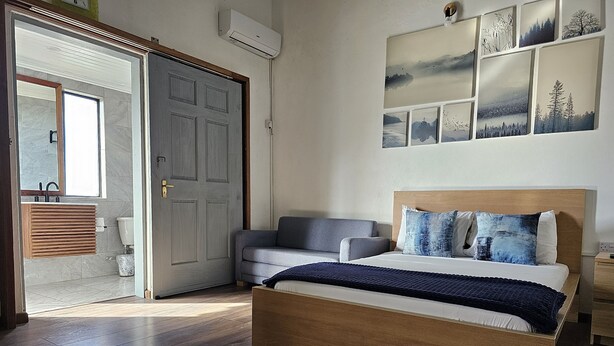 Une chambre à coucher avec un lit en bois, un canapé gris, une table de chevet en bois et un mur orné de tableaux.