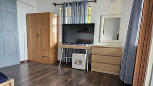 Une chambre avec une armoire en bois, un bureau avec une télévision et un petit réfrigérateur.