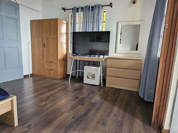 A room with a wooden wardrobe, a desk with a TV, and a small fridge. - Bay View Apartments - Canouan Island - Room 2A (Grenadines)