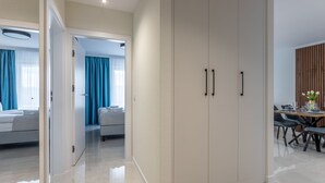 Quarto de hotel moderno com um guarda-roupa espaçoso, zona de refeições com mesa e cadeiras, e um quarto separado com cama e cortinas.