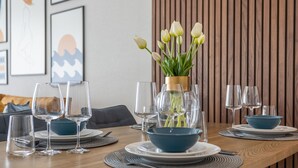 Mesa de jantar posta com tigelas azuis, copos de vinho e um vaso com tulipas brancas.