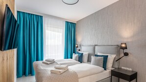 Quarto de hotel moderno com uma cama grande, mesa de cabeceira, abajur e vista para o exterior.