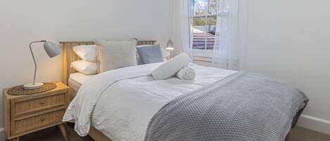 Una cama bien hecha con una manta gris, una lámpara de noche y una mesita de noche con cajones.