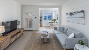 A modern living room with a flat-screen TV, a grey sofa, and a coffee table with a woven rug. - Luxe-Coastal Balmoral Beachfront (Mosman)