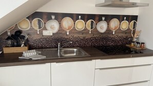 Una cocina moderna con encimera oscura, armarios blancos, un lavamanos de acero inoxidable y una zona de café con tazas variadas y una cafetera.